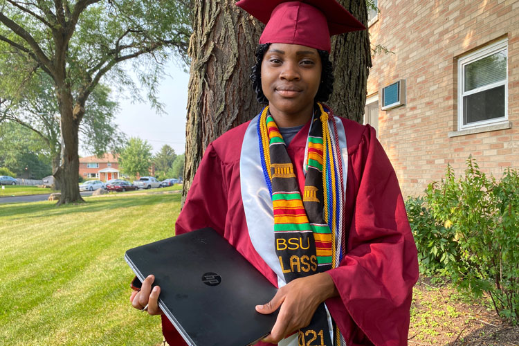 Jayda in cap and gown poses with her donated laptop from American Family Insurance