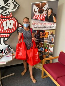Karen holding up gift bags in front of Bucky Badger cardboard cutout and Odyssey signage