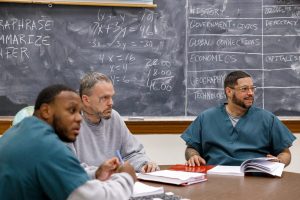 OBB students Billy, Danny and Mark sit at a table in a prison classroom and talk with with OBB director Peter Moreno in fall 2021