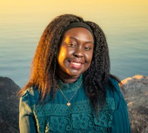 A smiling Josephine standing near a lake at sunset