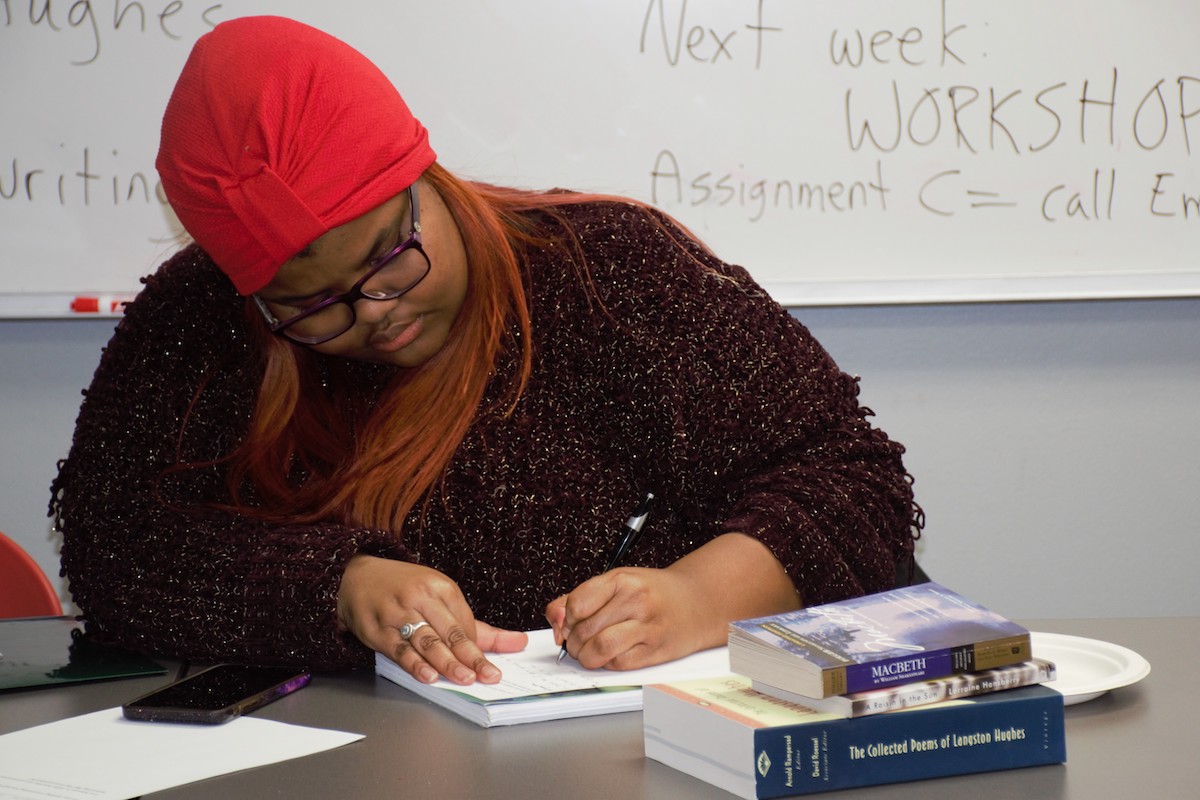 UW Odyssey Project alumni Loche Mothoa sits writing at a table with books