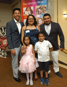Marisol, her husband and her children, standing in front of an Odyssey banner