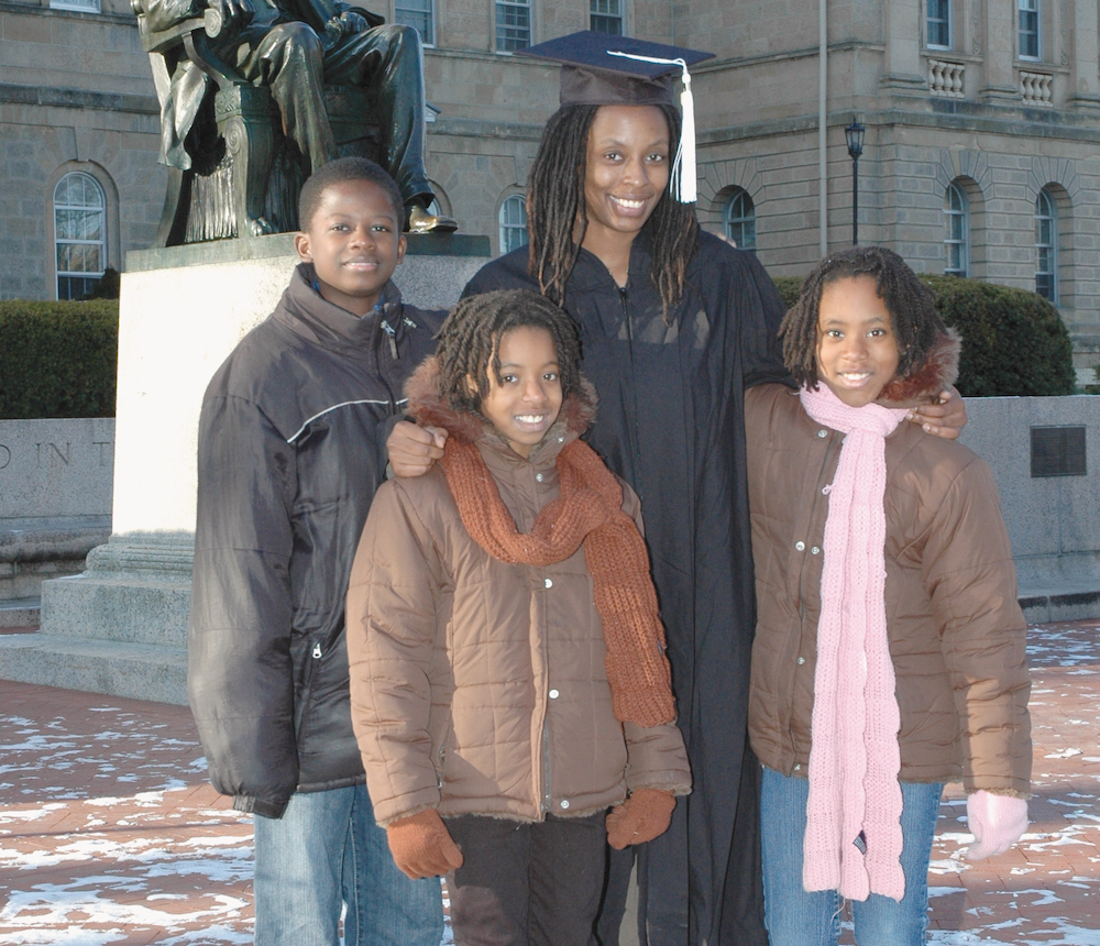 UW–Madison Odyssey Project graduate Kegan Carter stands in cap and gown with three youth.